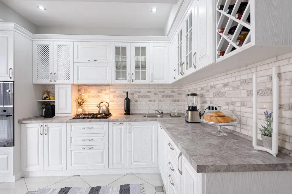 White kitchen remodeling design with classic cabinets, gray countertops, subway tile backsplash, and built-in wine rack.