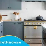 Kitchen cabinet hardware featuring black drawer pulls, brass oven knobs, and blue-gray cabinets in a modern kitchen.